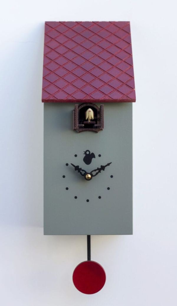 Cement grey (RAL7033) cuckoo clock with the appearance of a bird house. The clock has a red tile effect roof, black hands and dots for numbers and a red pendulum. A cuckoo appears from a little shuttered hole under the eaves of the roof