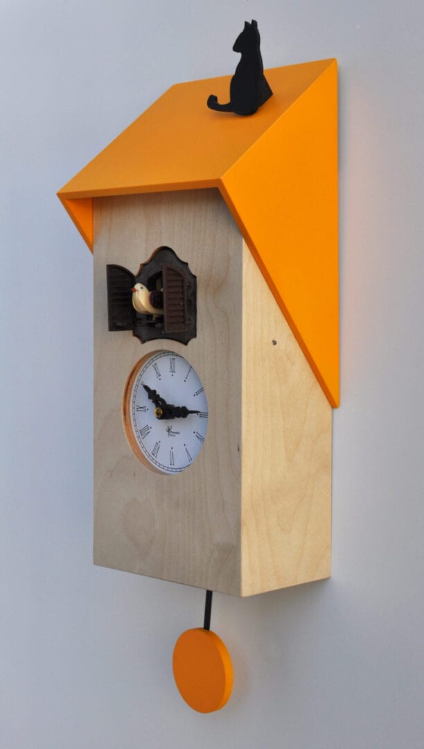 A natural wood clock with a bright yellow roof on which sits a black cat. The cuckoo emerges from a black door just above the clock face