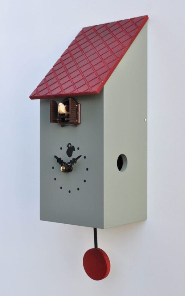 Viewed from the right hand side, a grey coloured MDF cuckoo clock in the style of a birdhouse, with a little house for the cuckoo just under the roof, black hands and dots for numbers and a pendulum