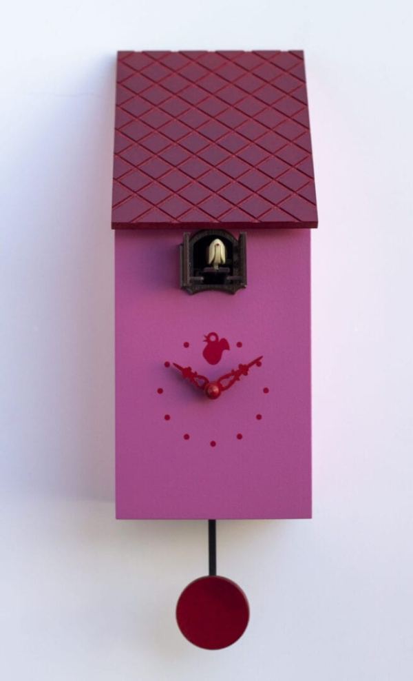 A pink cuckoo clock in the form of a bird house with a red rood and pendulum, and hands. The cuckoo appears from a little home under the eaves