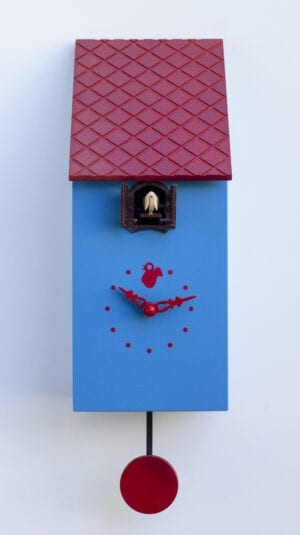 A cute blue cuckoo clock which looks like a bird house. The clock has red hands and dots for numbers, with a little cuckoo house just under the eaves of the red roof.
