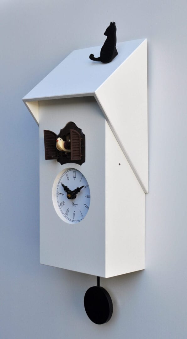 Side view of a white mdf cuckoo clock with white roof, topped by a cat
