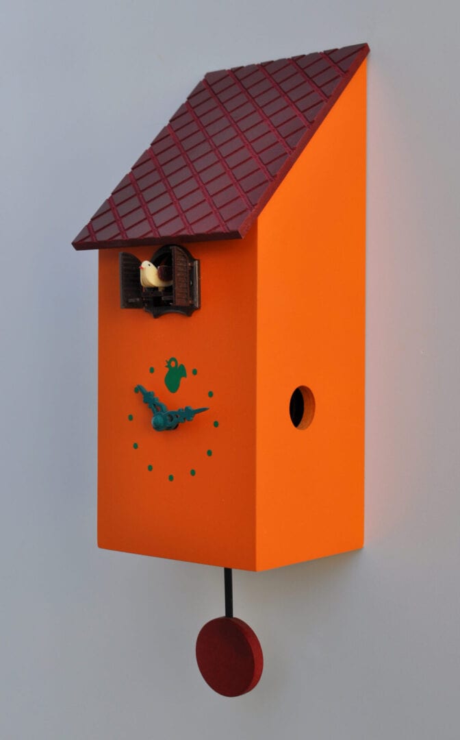 A birdhouse cuckoo clock in orange with a burgundy roof.