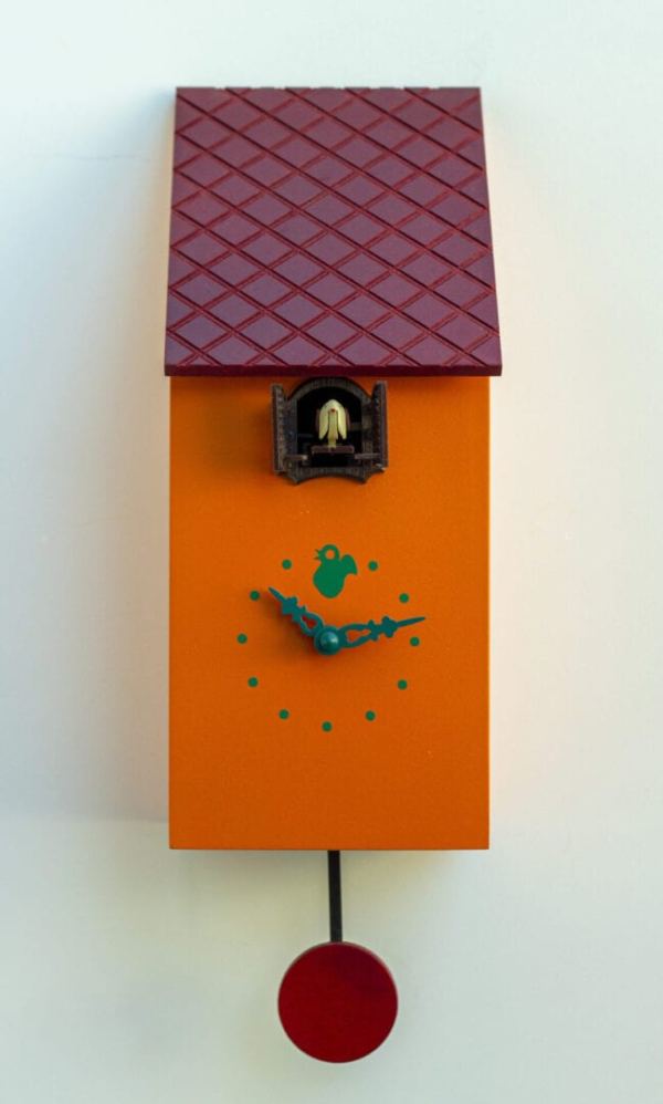 Orange clock shaped like a bird house, with a burgundy roof which appears to be tiled. The cuckoo appears from a little hole justs under the eaves.