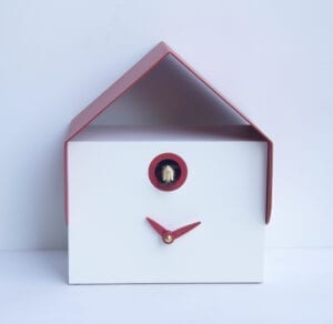 Image shows a small rectangular wall or desk cuckoo clock in white mdf with a red metal room and red hands. The cuckoo peeps our from a small hole under the roof, which is also trimmed in red