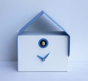 The Dotto Cuckoo clock in white MDF with small blue hands under the cuckoo's house, which is also trimmed in blue. The clock has a thin metal roof, also in blue