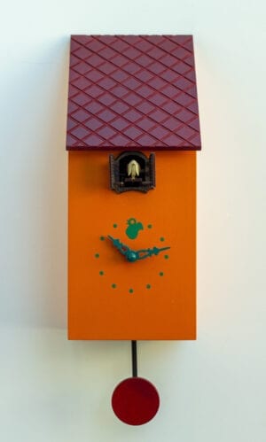 Orange clock shaped like a bird house, with a burgundy roof which appears to be tiled. The cuckoo appears from a little hole justs under the eaves.