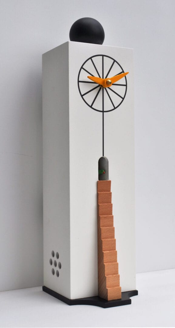 Left hand view of the Ziggurat cuckoo clock, showing white MDF rectantular box-like case, with beechwood ladder leading to the cuckoo house, with a wheel type face with orange hands for telling the time