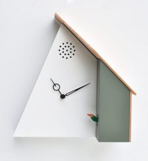 House 78, part of the QQ range of clocks, where the clock takes the form of a reimagined house, from which the cuckoo appears laterally rather than from the front of the clock, thereby giving a different persepective. The clock is in white and cement grey, with a wooden roof.