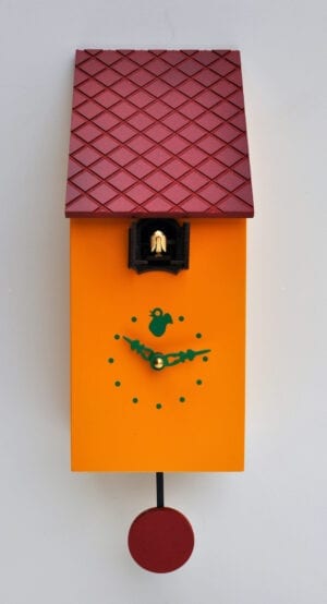 A rectangular cuckoo clock in orange-yellow with a burgundy red textured roof, burgundy pendulum and green detail on the clock face. A cuckoo appears from its hole under the roof.