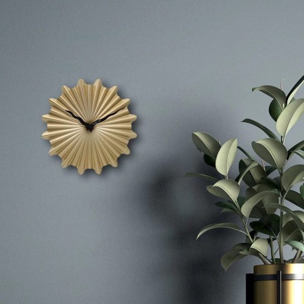Gold Sunny wall clock set against a grey wall with a plant in the foreground.