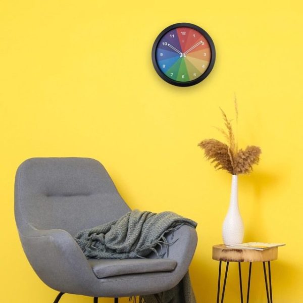 Rainbow coloured Joy wall clock shown against a yellow wall in a room setting