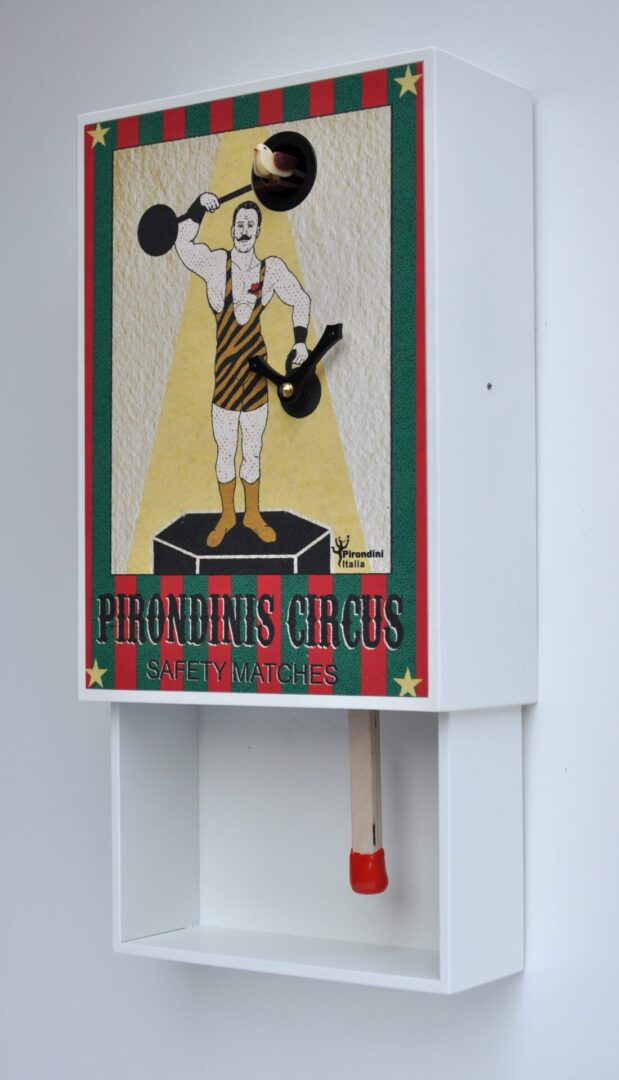 Circus themed cuckoo clock showing a 'strong man' lifting weights, one of which holds the cuckoo.